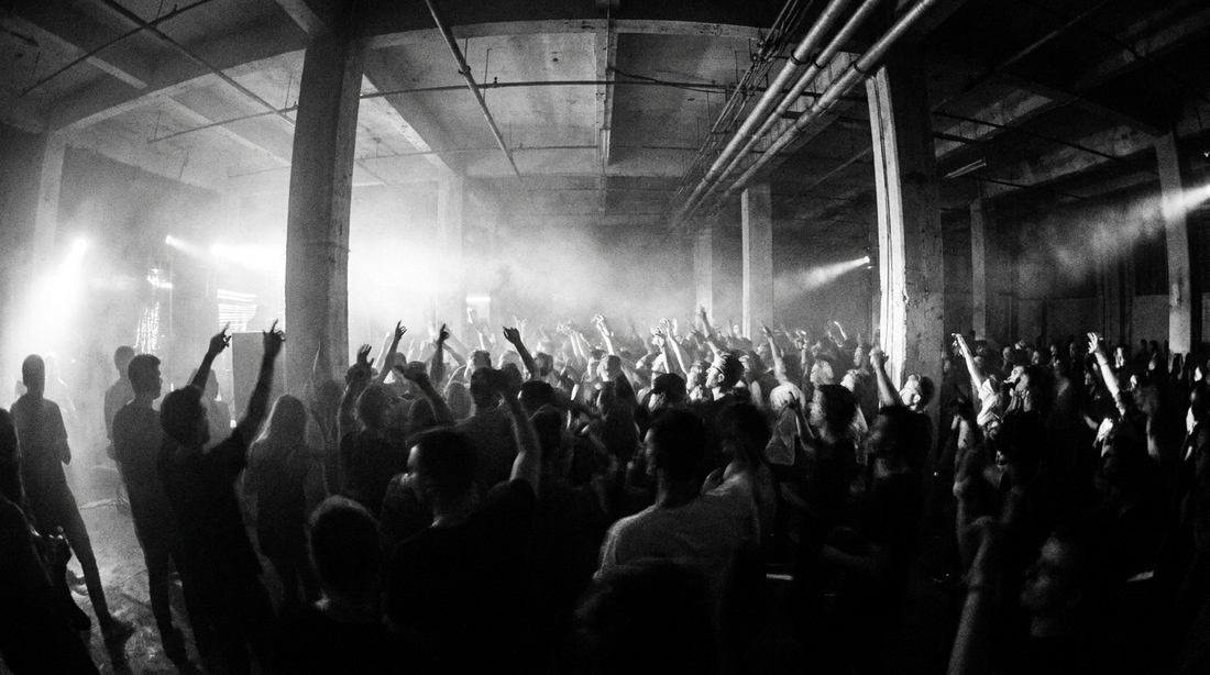 Rave in einer Industriehalle mit Menschenmenge und Stroboskoplicht