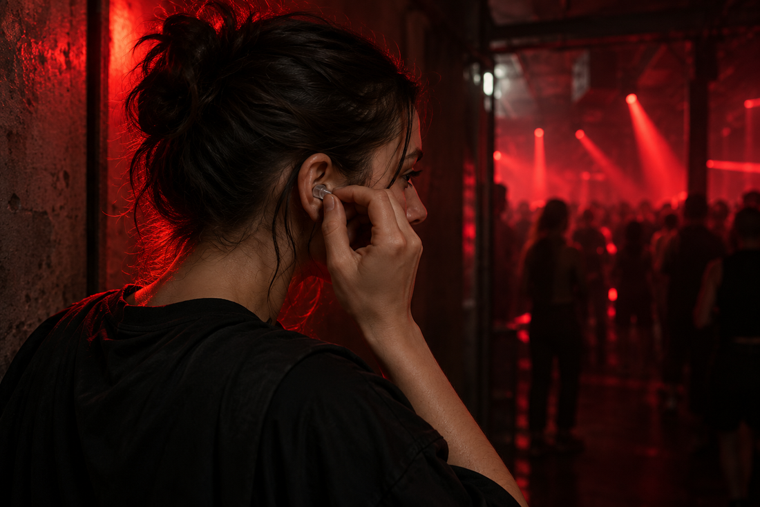 Eine Raverin setzt vor einer rot beleuchteten Tanzfläche einen transparenten Ohrstöpsel ein